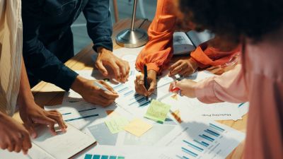 Team arbeitet gemeinsam an Projektmanagement-Dokumenten mit Diagrammen und Notizen auf einem Schreibtisch. 