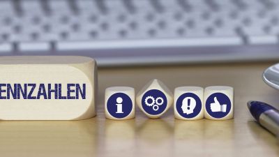 Holzwürfel mit Icons für Informationen, Prozesse, Warnhinweise und Bewertungen stehen neben einem Block mit der Aufschrift „Kennzahlen“ und zeigen die Bedeutung von KPIs im IT-Management. 