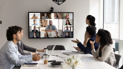 Hybrides Meeting im modernen Büro: Team vor großem Bildschirm in Videokonferenz. 