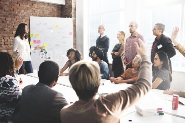 Diverse Projektgruppe bei einem interaktiven Meeting mit Whiteboard und Diskussion. Ein Beispiel für Teamkommunikation.