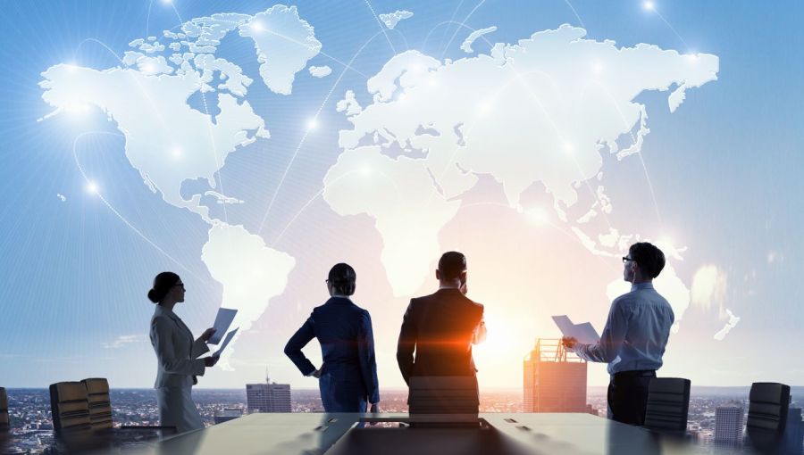 Vier Geschäftsleute in einem Meeting, im Hintergrund eine Weltkarte: Symbol für internationales Projektmanagement und globale Zusammenarbeit.