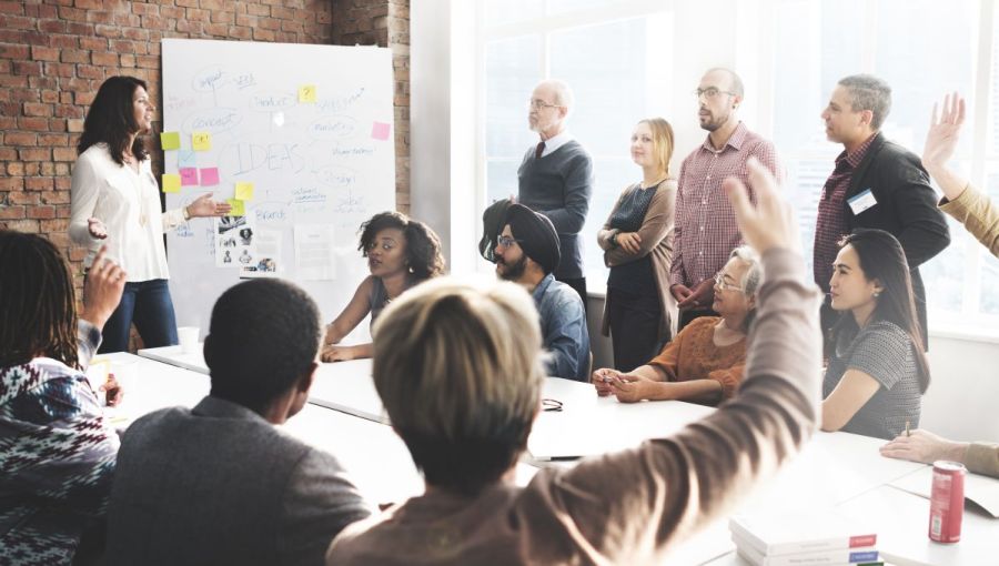 Diverse Projektgruppe bei einem interaktiven Meeting mit Whiteboard und Diskussion. Ein Beispiel für Teamkommunikation.